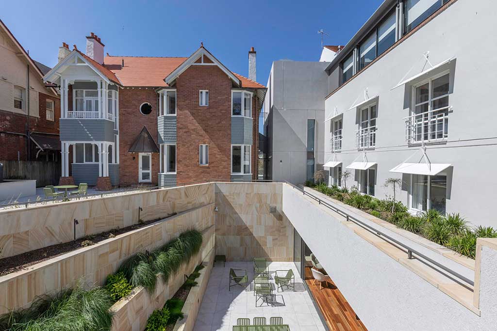 External view of the backyard space of the Coombs Centre. The heritage listed residence is on the left and the newer building on the right. The breakout space on level 1 is sunk in the middle of the image.